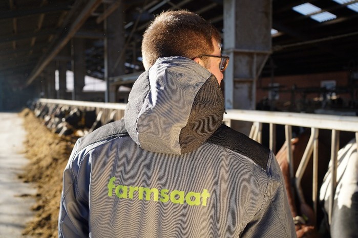 Ein Bauer in einem Kuhstall trägt eine Jacke mit der Aufschrift farmsaat
